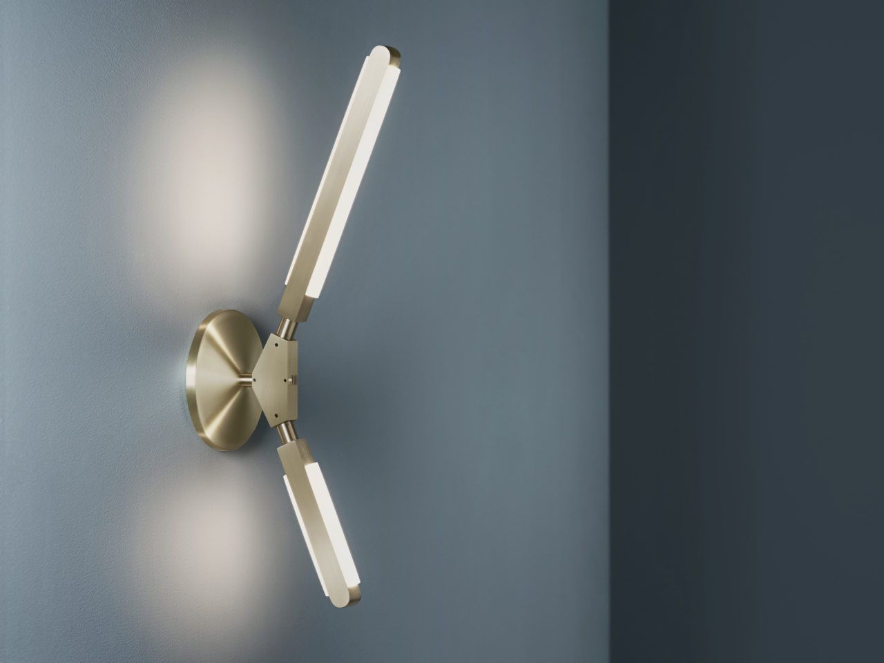 Three quarter view of an illuminated Pris K sconce with satin brass metal components.