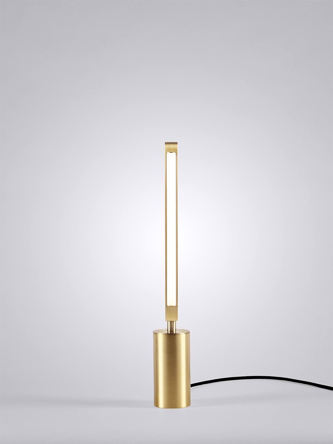 Front view of an illuminated Pris table lamp with satin brass metal components.