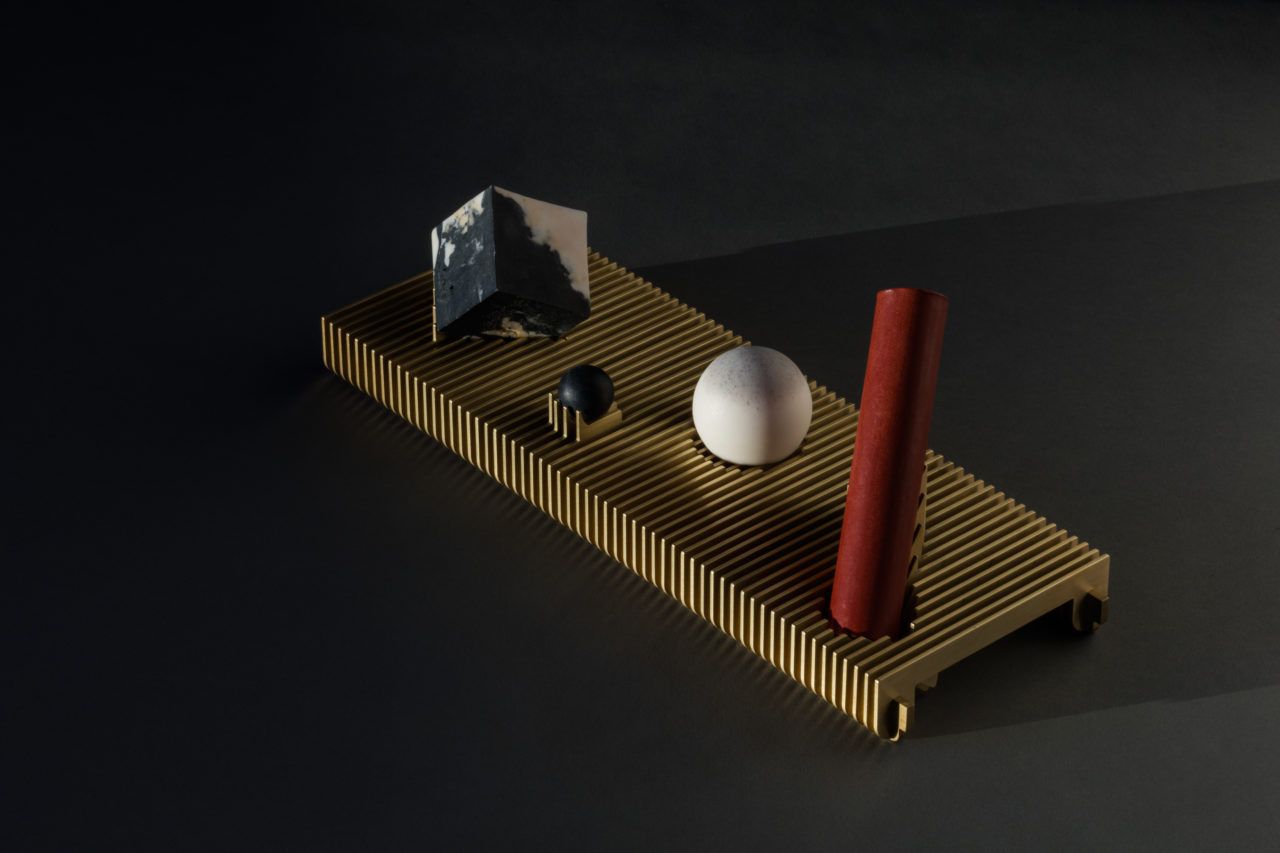 A set of four soaps in classic geometric shapes: cube, sphere, and cylinder. They sit on a ribbed brass tray with supports custom fit to each soap.
