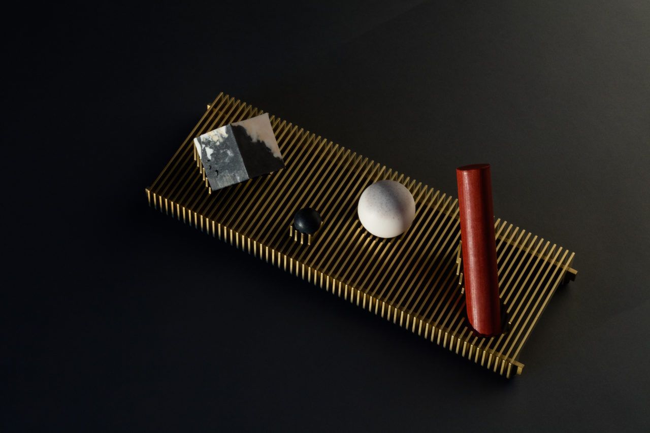 A set of four soaps in classic geometric shapes: cube, sphere, and cylinder. They sit on a ribbed brass tray with supports custom fit to each soap.