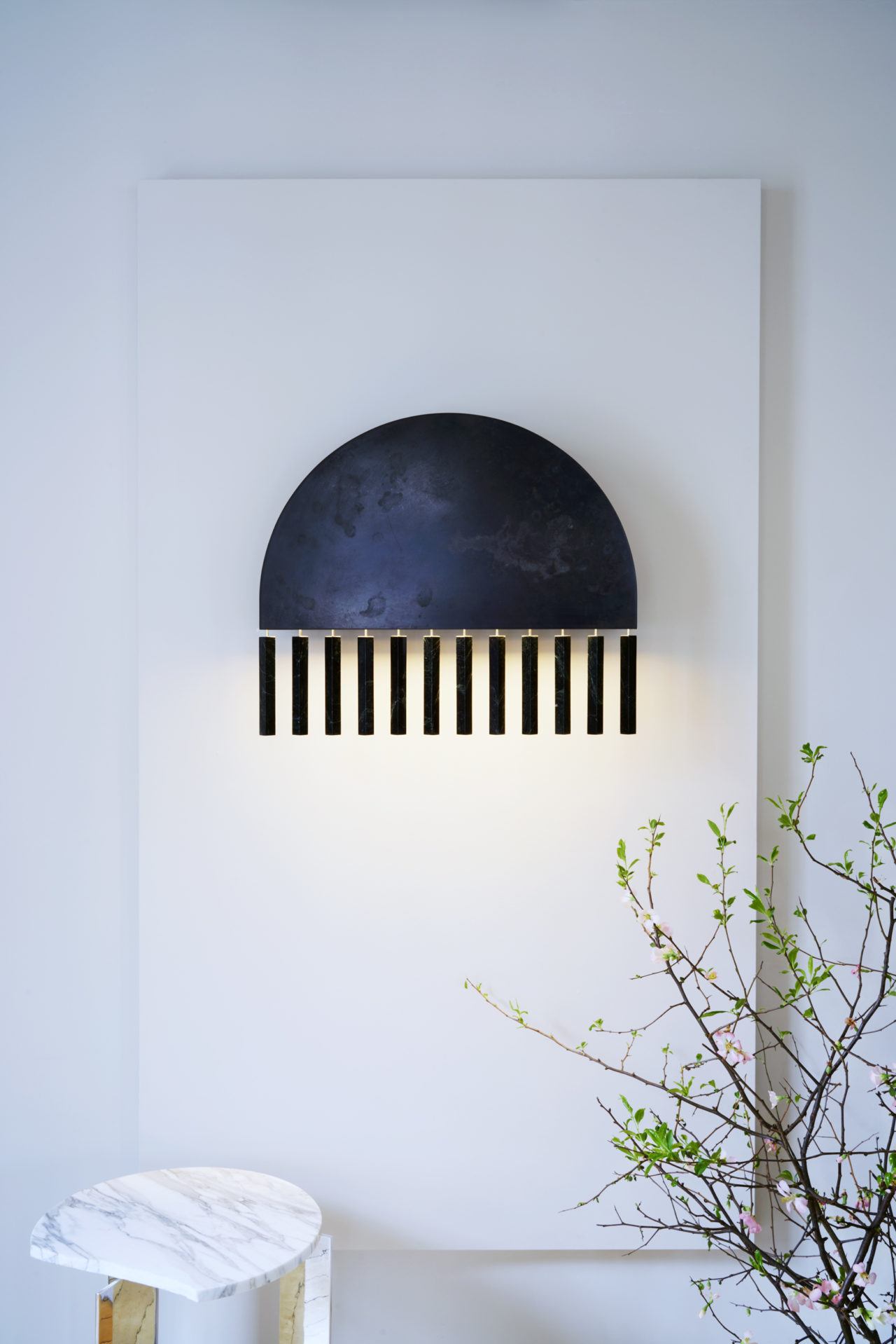 Pelle’s Dark Moon Wall Sconce hangs on a white wall above their Lost and Found side table.