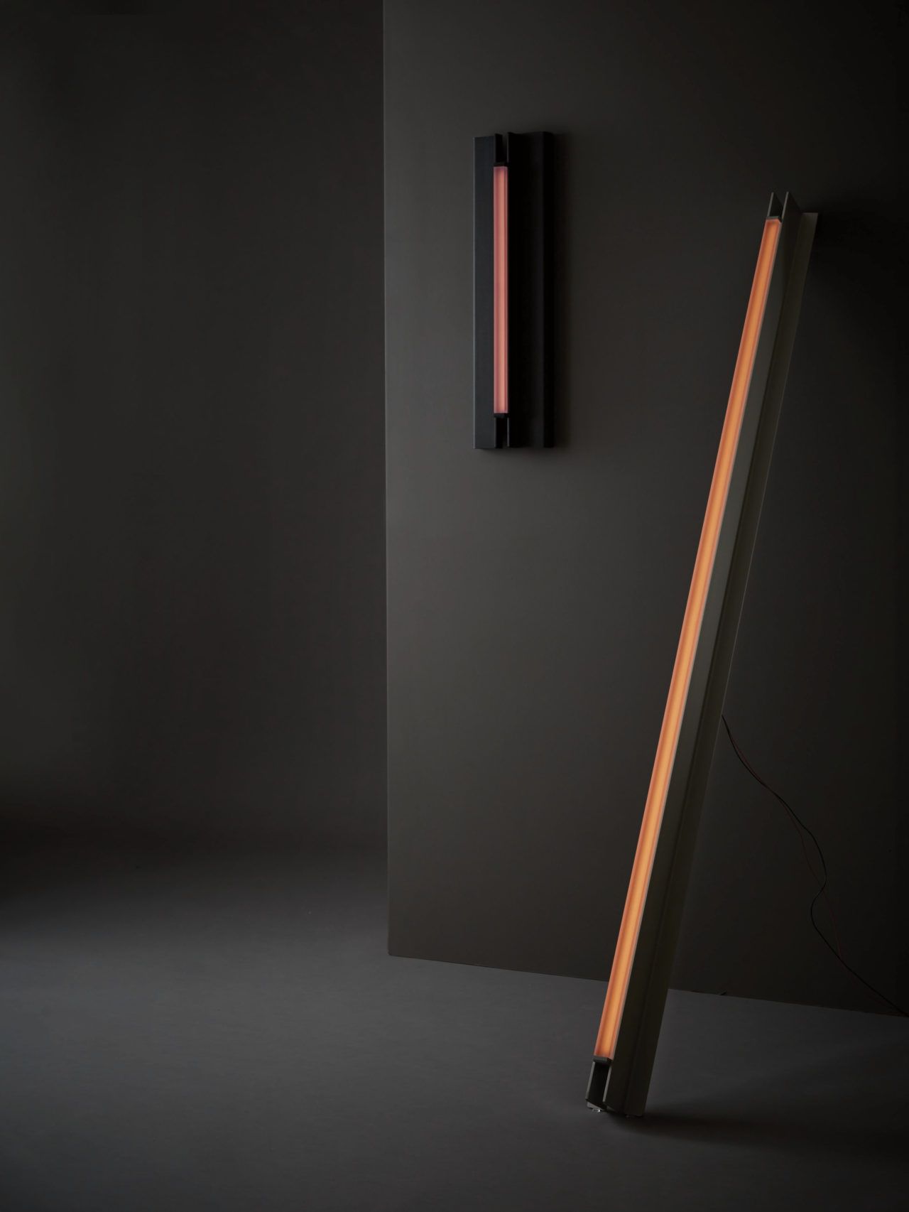 Two of Pelle’s colorful Beam and Glow pendants, a Glow 02 Sconce and a Beam 06 Sconce are displayed in a dark gray room.
