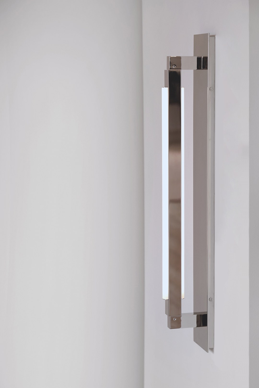 Side view of an illuminated Pris Bar sconce with reflective polished nickel metal components.