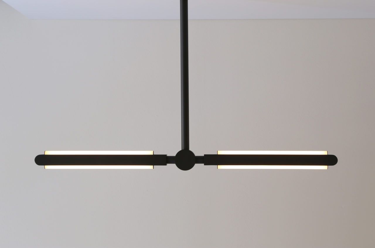 Side view of an illuminated Pris Linear pendant with black brass metal components.