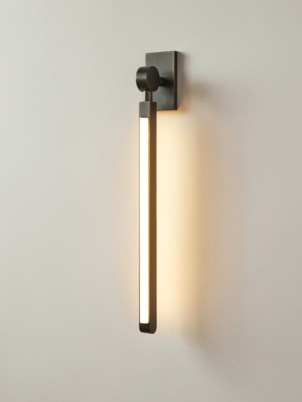 An illuminated Pris I Sconce with dark bronze metal components.