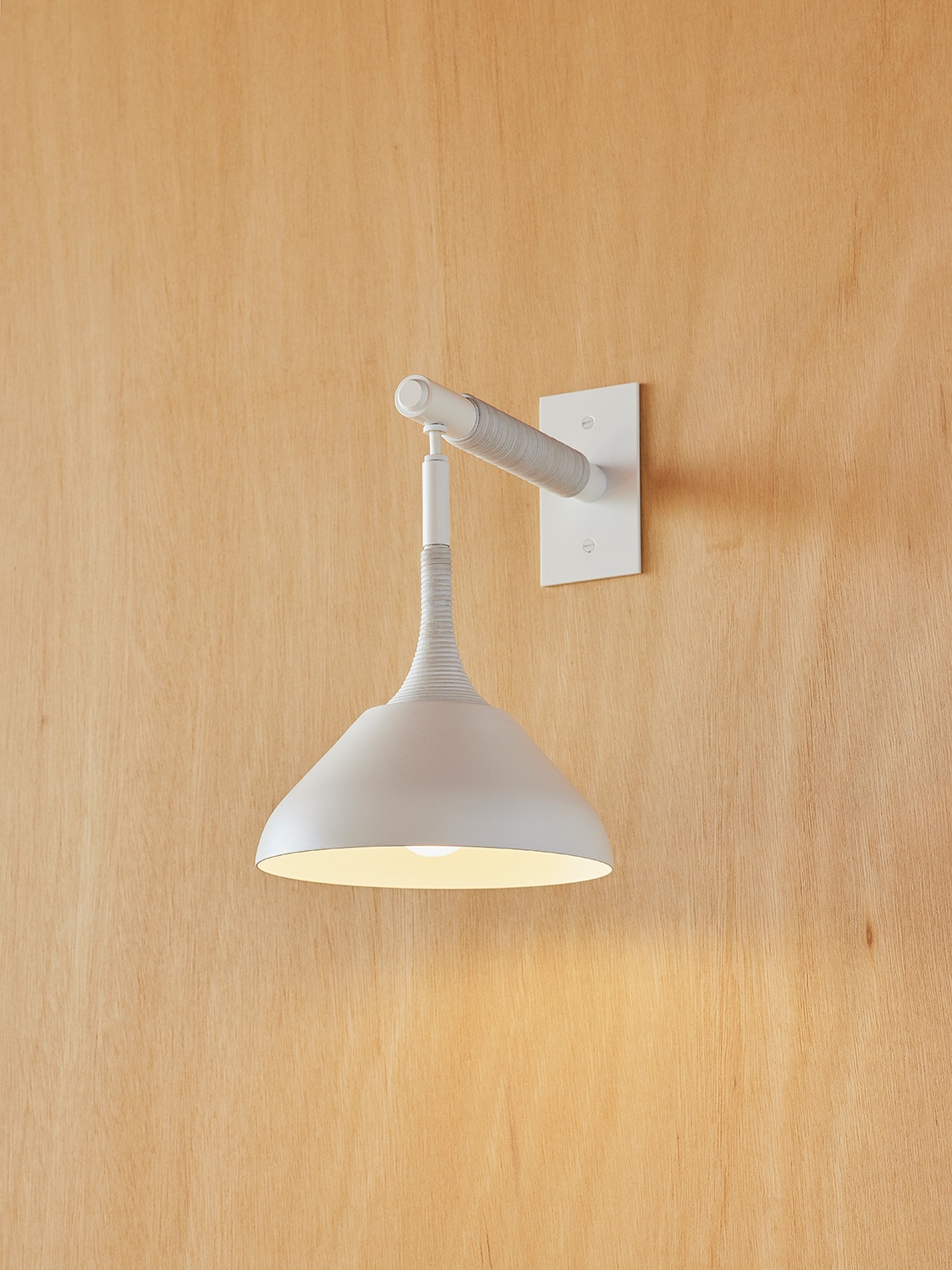 Pelle’s Stem Shade Mini Sconce in white powder coat with white leather coiling hangs against a light wood wall.
